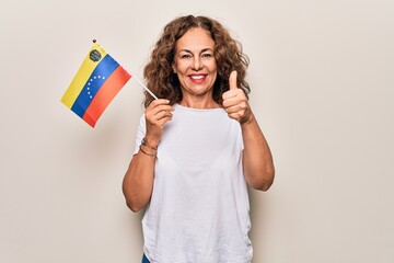 Middle age beautiful tourist woman holding venezuelan flag over isolated white background smiling happy and positive, thumb up doing excellent and approval sign