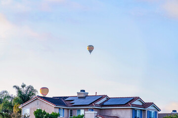 Fototapeta na wymiar Colorful hot air balloons against cloudy blue sky over house with solar panels