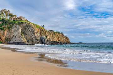 Fototapeta na wymiar Shore and ocean by a rocky cliff against cloudy sky in Laguna Beach California