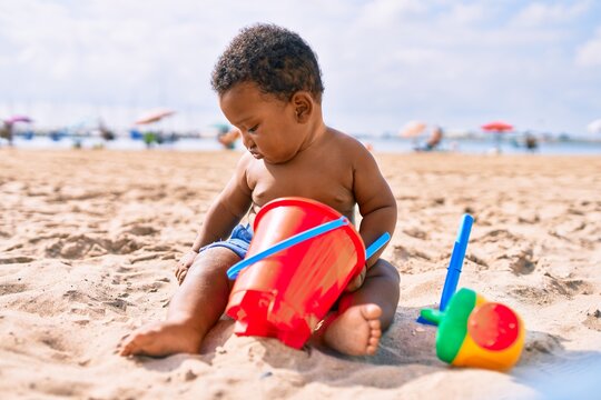 Adorable african american toddler playing with toys sitting on the sand at the beach.