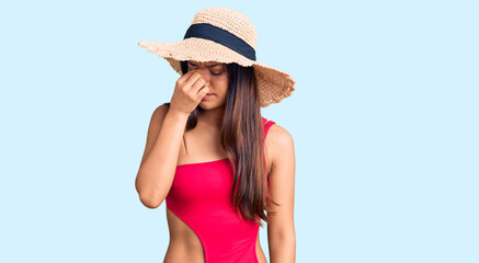 Young beautiful latin girl wearing swimwear and summer hat tired rubbing nose and eyes feeling fatigue and headache. stress and frustration concept.