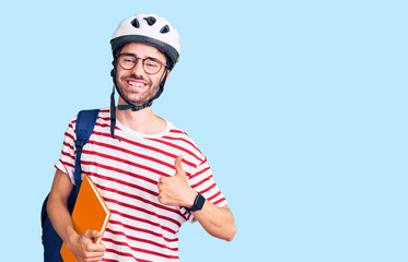 Young hispanic man wearing student backpack and bike helmet holding binder smiling happy and positive, thumb up doing excellent and approval sign
