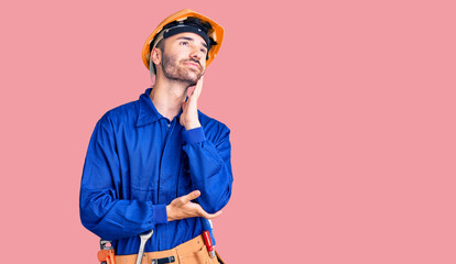 Young hispanic man wearing worker uniform with hand on chin thinking about question, pensive expression. smiling and thoughtful face. doubt concept.