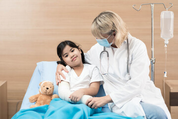 Portrait of smile doctor pediatrician and little girl patient on the bed with teddy bear