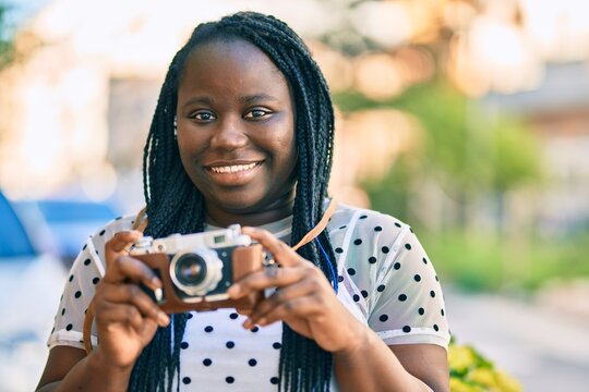 Young african american tourist woman smiling happy using vintage camera at the city.