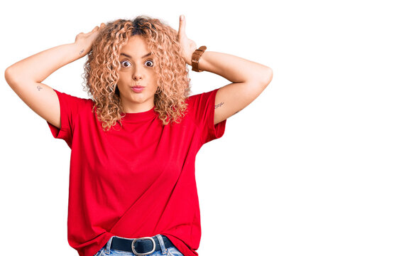 Young blonde woman with curly hair wearing casual red tshirt doing bunny ears gesture with hands palms looking cynical and skeptical. easter rabbit concept.