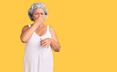 Senior woman with gray hair wearing casual clothes smelling something stinky and disgusting, intolerable smell, holding breath with fingers on nose. bad smell