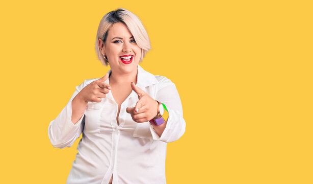 Young blonde plus size woman wearing casual shirt pointing fingers to camera with happy and funny face. good energy and vibes.