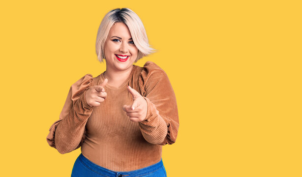 Young blonde plus size woman wearing casual sweater pointing fingers to camera with happy and funny face. good energy and vibes.