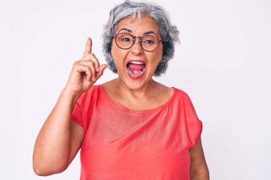 Senior hispanic grey- haired woman wearing casual clothes and glasses pointing finger up with successful idea. exited and happy. number one.