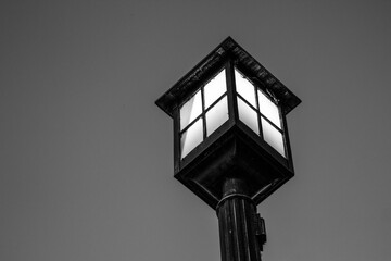 Fototapeta na wymiar Old fashioned lamp post illuminated against the night sky. Black and white in horizontal orientation with copy space. 