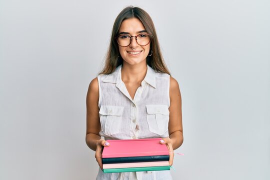 Young hispanic woman holding books smiling with a happy and cool smile on face. showing teeth.