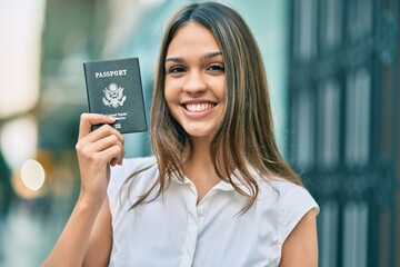 Beautiful latin teenager girl smiling happy holding united states passport at the city.