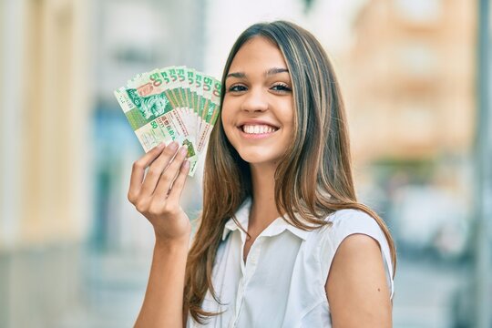 Beautiful latin teenager girl smiling happy holding hong kong dollars at the city.