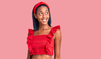 Young african american woman wearing casual summer clothes looking away to side with smile on face,...