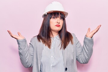 Young plus size woman wearing architect hardhat clueless and confused with open arms, no idea and doubtful face.