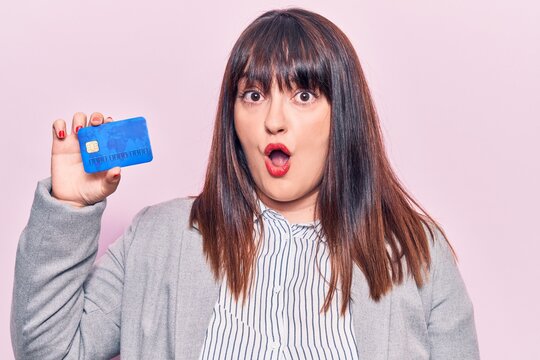 Young plus size woman holding credit card scared and amazed with open mouth for surprise, disbelief face