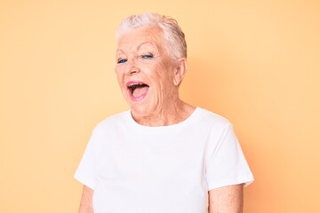 Senior beautiful woman with blue eyes and grey hair wearing classic white tshirt over yellow...
