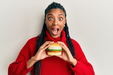 African american woman with braids eating hamburger celebrating crazy and amazed for success with...