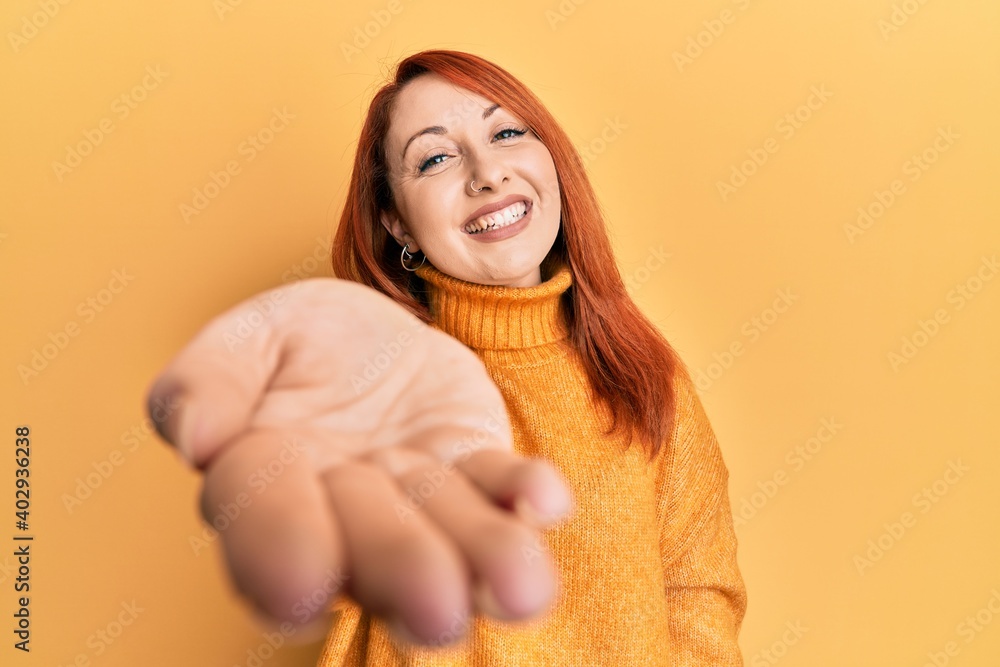 Poster beautiful redhead woman wearing casual winter sweater over yellow background smiling cheerful offeri