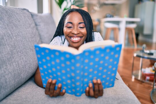 Young african american woman smiling happy laying on the sofa reading book at home