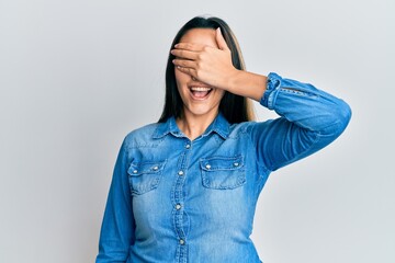 Young hispanic woman wearing casual denim jacket smiling and laughing with hand on face covering eyes for surprise. blind concept.