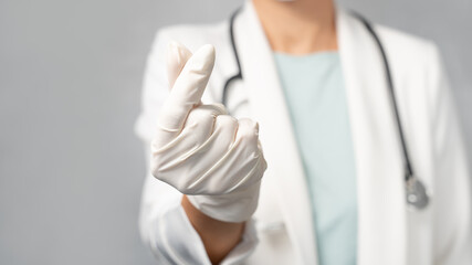 A professional female doctor in white gown with stethoscope and protective gloves making finger heart gesture to support the frontlines healthcare workers team and everyone. Fighting agaist Covid 19.