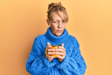 Middle age blonde woman drinking a cup coffee skeptic and nervous, frowning upset because of problem. negative person.