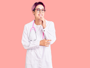 Young beautiful woman with pink hair wearing doctor uniform looking confident at the camera with smile with crossed arms and hand raised on chin. thinking positive.