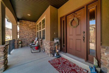 Brown door with sidelights and wreath at house facade with open front porch