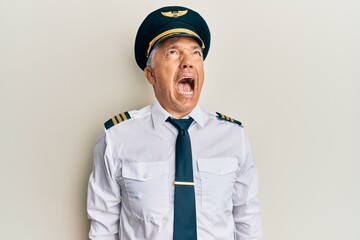 Handsome middle age mature man wearing airplane pilot uniform angry and mad screaming frustrated...