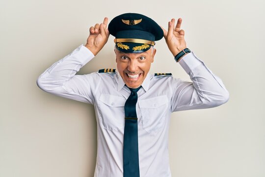Handsome middle age mature man wearing airplane pilot uniform posing funny and crazy with fingers on head as bunny ears, smiling cheerful