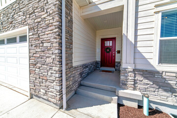 House facade with vibrant red front door attached garage and stone brick wall