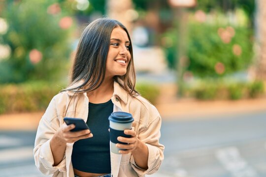 Young hispanic girl smiling happy using smartphone and drinking take away coffee at the park.