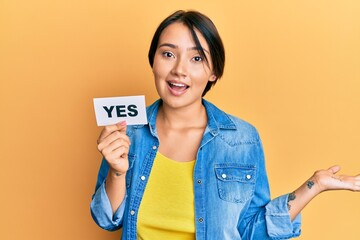 Beautiful young woman with short hair holding yes reminder celebrating achievement with happy smile...