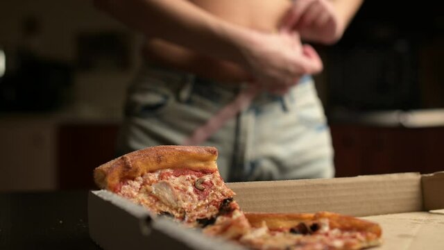 Focus moves from leftover pizza on table to young woman measuring waist. Selective focus