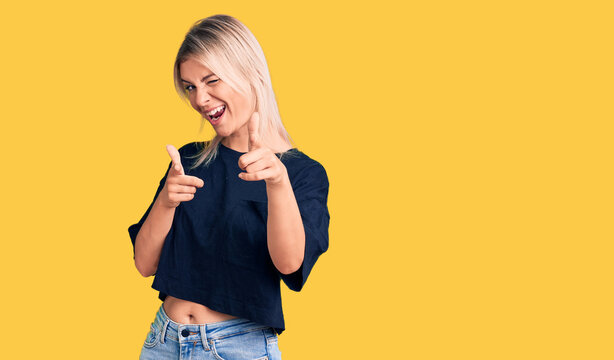 Young beautiful blonde woman wearing casual t-shirt pointing fingers to camera with happy and funny face. good energy and vibes.