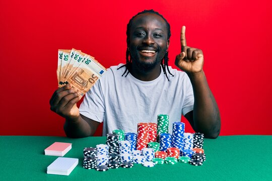 Handsome young black man playing poker holding 50 euros banknotes smiling with an idea or question pointing finger with happy face, number one