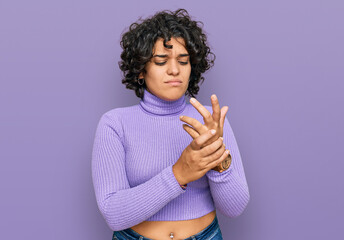 Young hispanic woman with curly hair wearing casual clothes suffering pain on hands and fingers,...