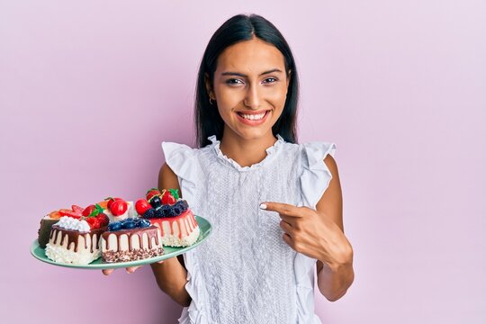 Young brunette woman holding cake slices smiling happy pointing with hand and finger
