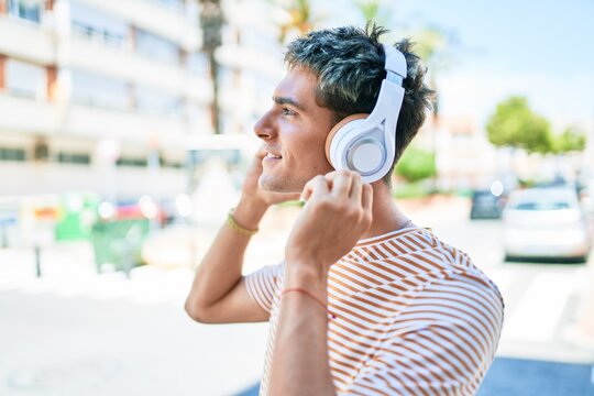 Young handsome caucasian man smiling happy listening to music using headphones walking at city.