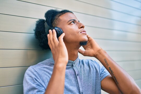 Young african american man with unhappy expression listening to music using headphones at the city.