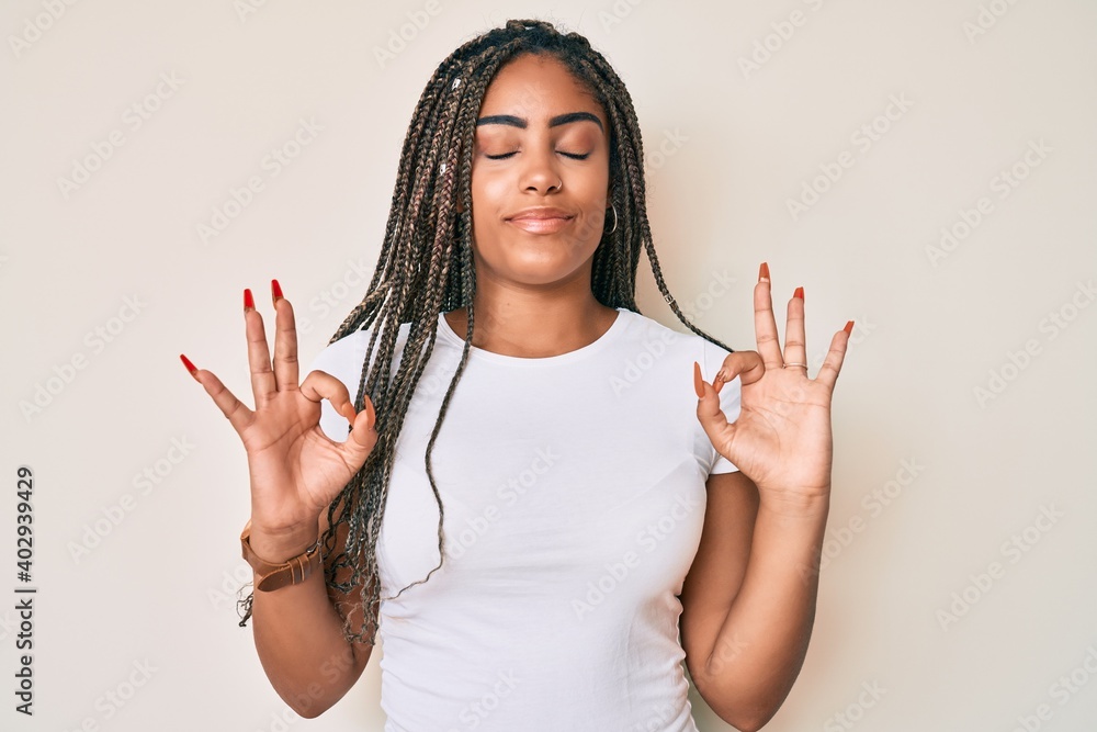 Wall mural Young african american woman with braids wearing casual white tshirt relax and smiling with eyes closed doing meditation gesture with fingers. yoga concept.