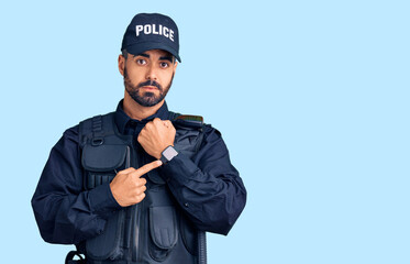 Obraz premium Young hispanic man wearing police uniform in hurry pointing to watch time, impatience, looking at the camera with relaxed expression