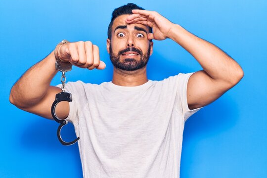 Young hispanic man holding prisoner handcuffs stressed and frustrated with hand on head, surprised and angry face