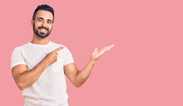 Young hispanic man wearing casual clothes amazed and smiling to the camera while presenting with hand and pointing with finger.