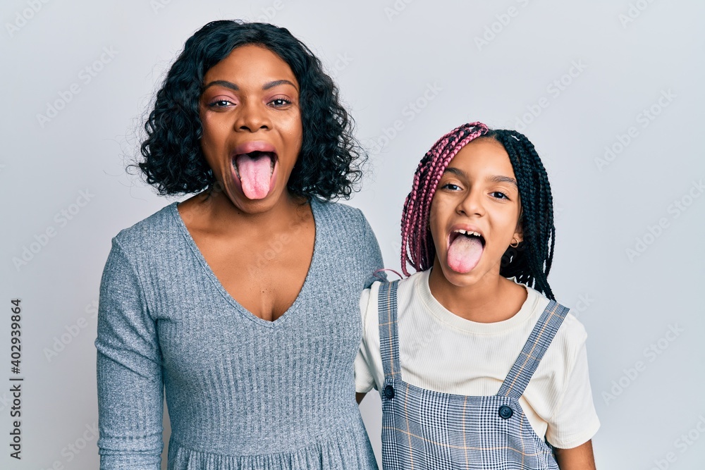 Sticker Beautiful african american mother and daughter wearing casual clothes and hugging sticking tongue out happy with funny expression. emotion concept.