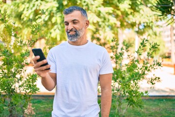 Middle age grey-haired man smiling happy using smartphone at the park
