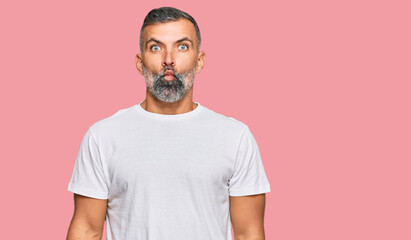 Middle age handsome man wearing casual white tshirt making fish face with lips, crazy and comical gesture. funny expression.