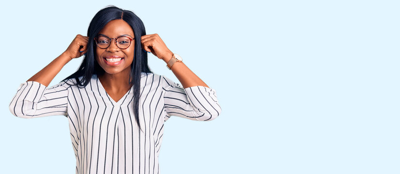 Young african american woman wearing casual clothes and glasses smiling pulling ears with fingers, funny gesture. audition problem